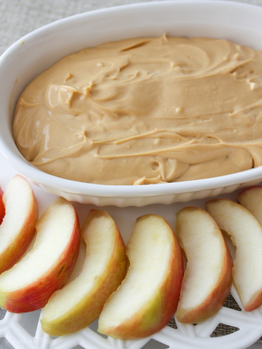 Caramel apple dip in a white bowl surrounded by apple slices. 