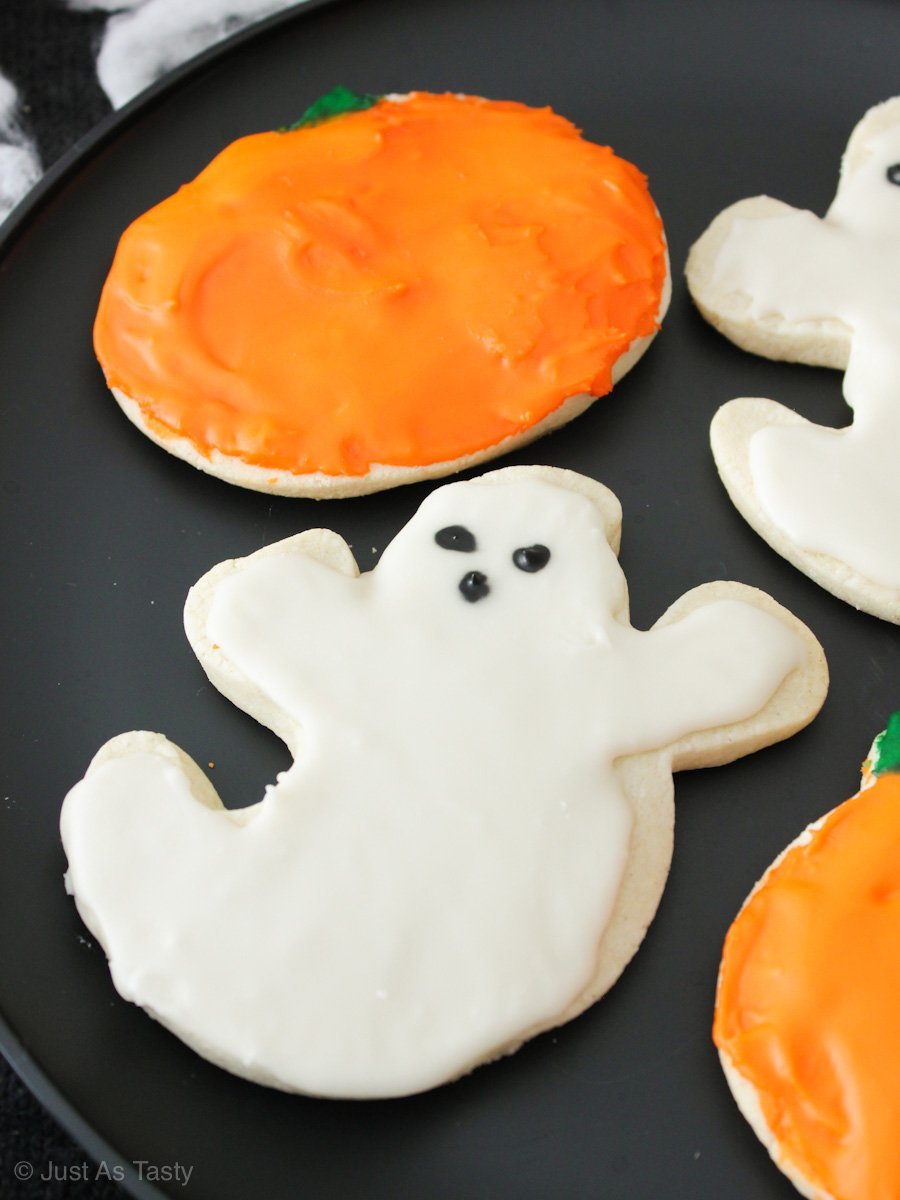 Close-up of frosted ghost and pumpkin shaped Halloween sugar cookies on a black plate. 