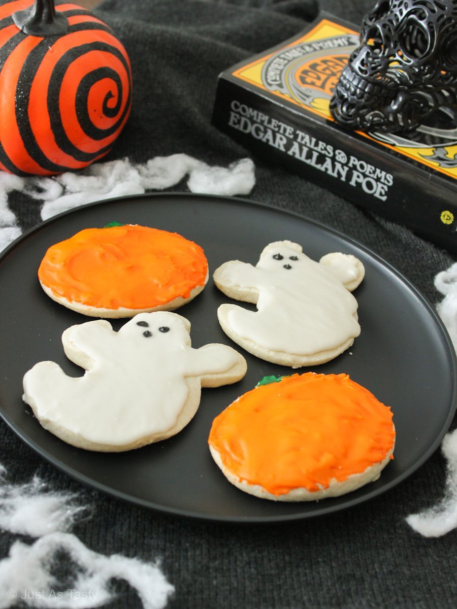 Frosted ghost and pumpkin shaped Halloween sugar cookies on a black plate. 