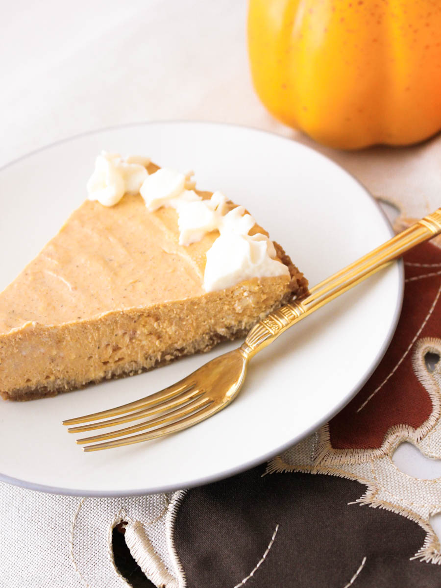 Slice of pumpkin cheesecake on a white plate with a gold fork.