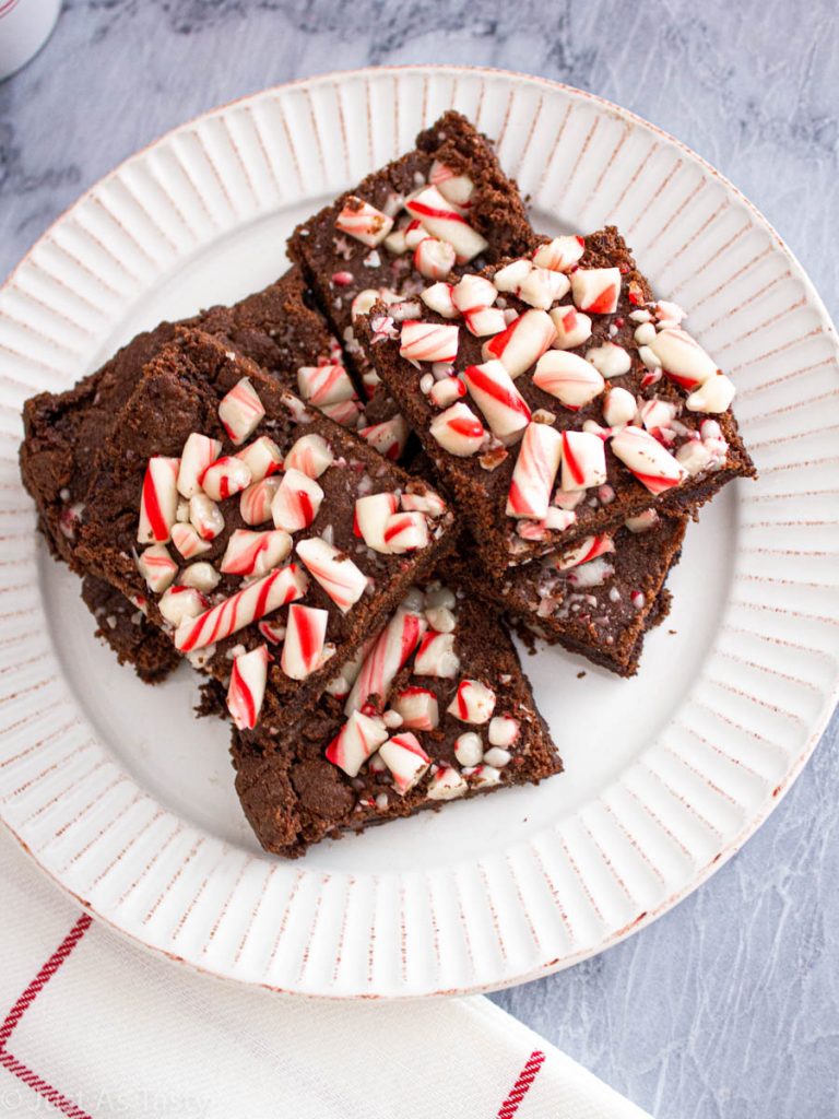 Peppermint brownies topped with candy canes on a white plate. 