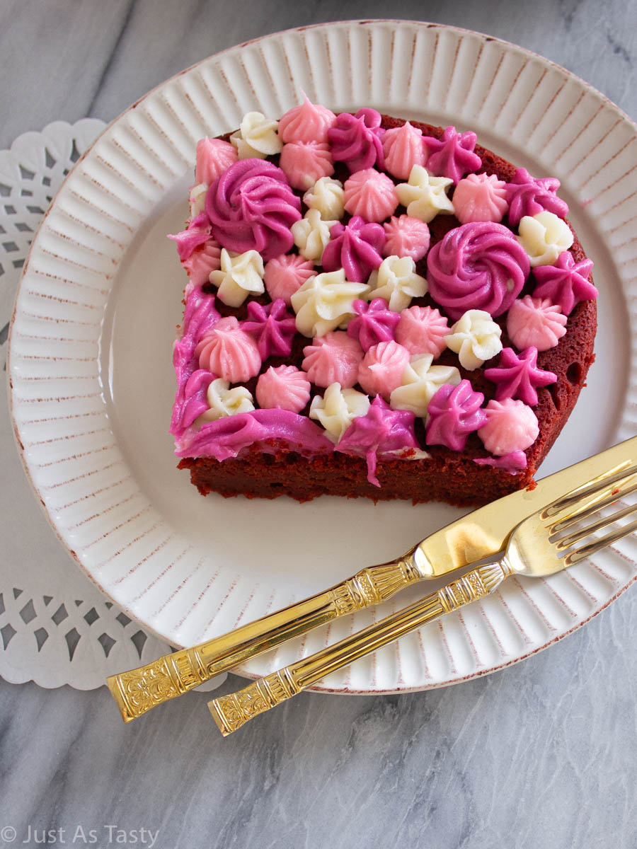 Slice of gluten free red velvet cake with pink and white piped frosting on top.