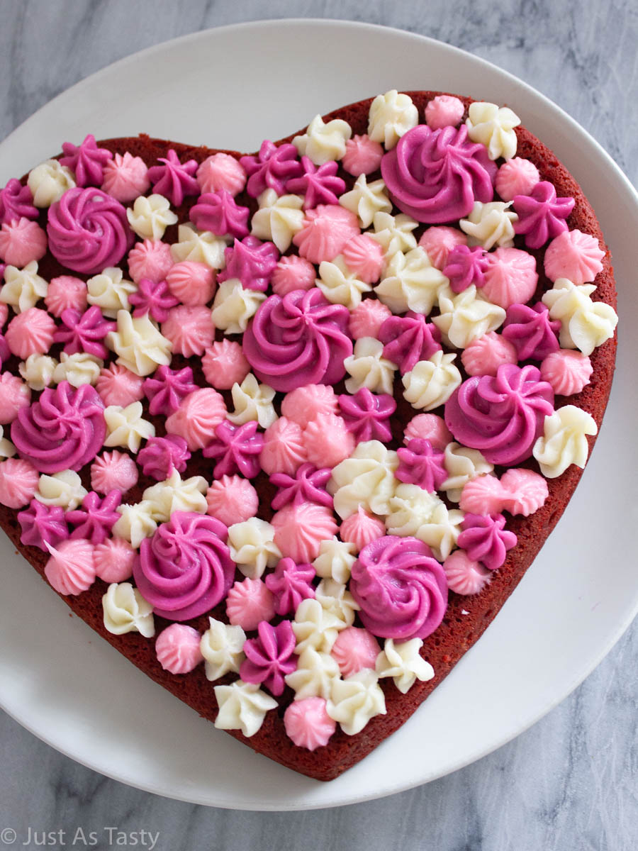 Heart shaped gluten free red velvet cake with pink and white piped frosting on top.