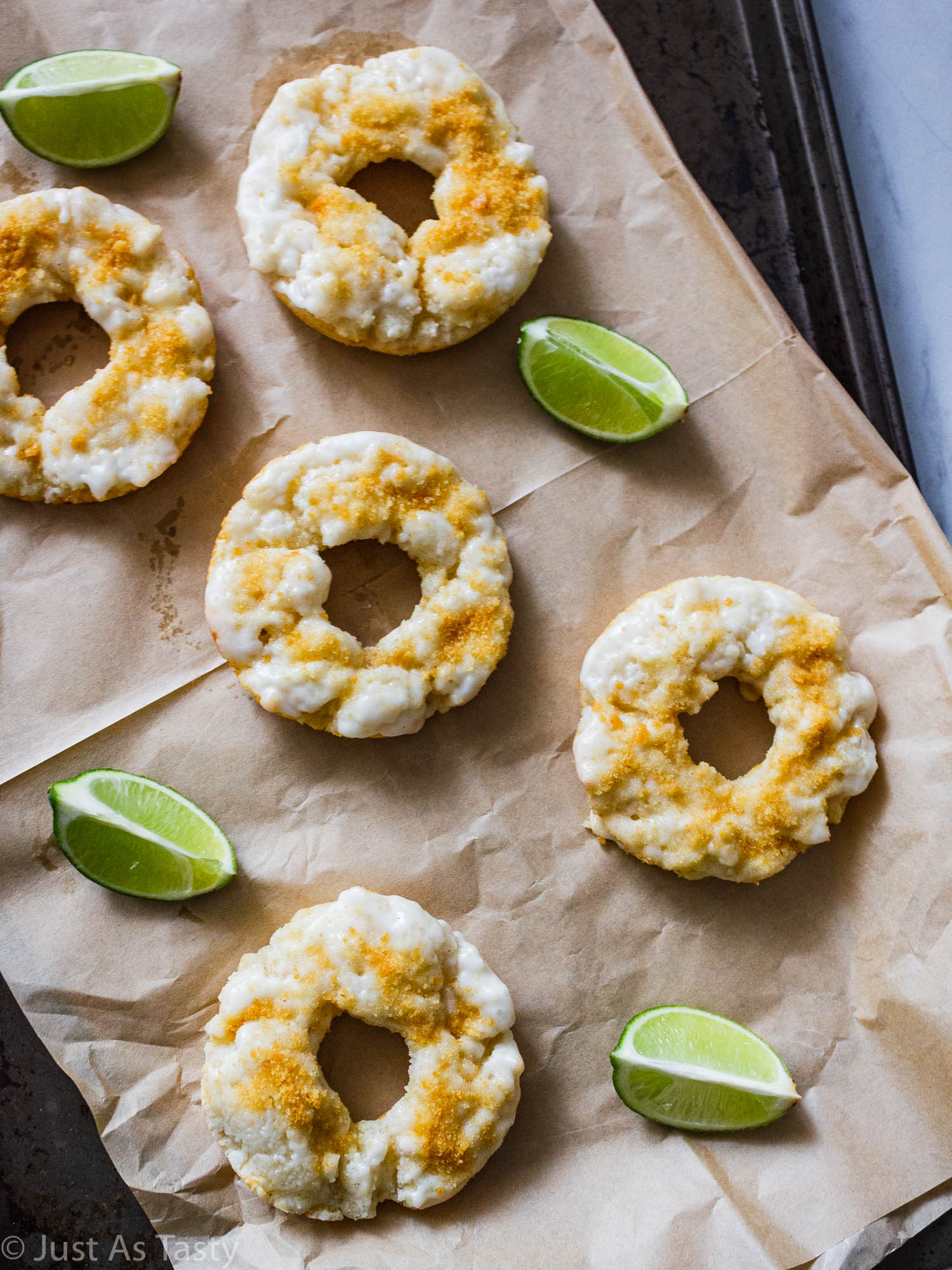 Glazed key lime donuts on parchment paper surrounded by lime wedges.