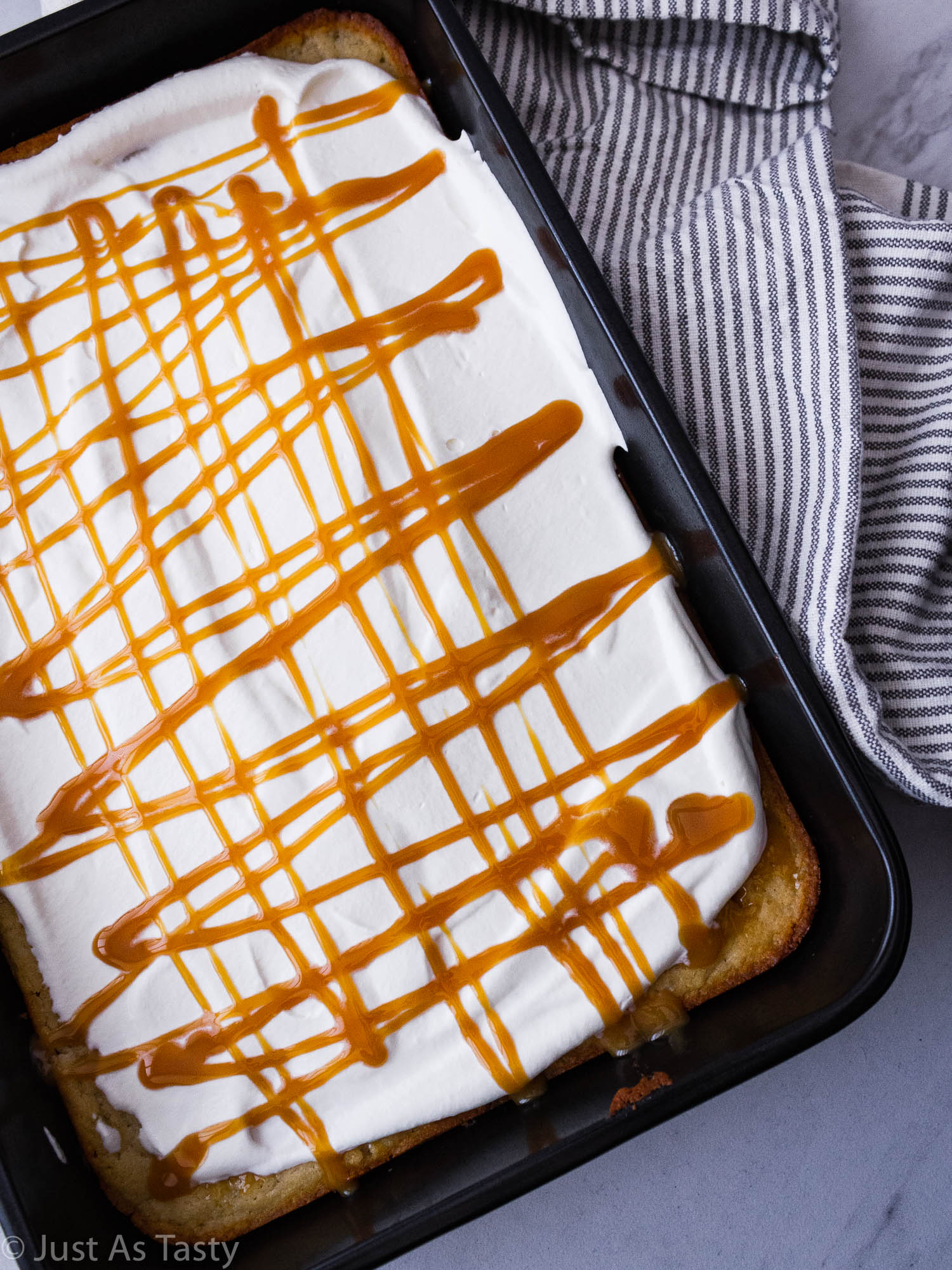 Caramel cake topped with whipped cream and a drizzle of caramel sauce in a cake pan.