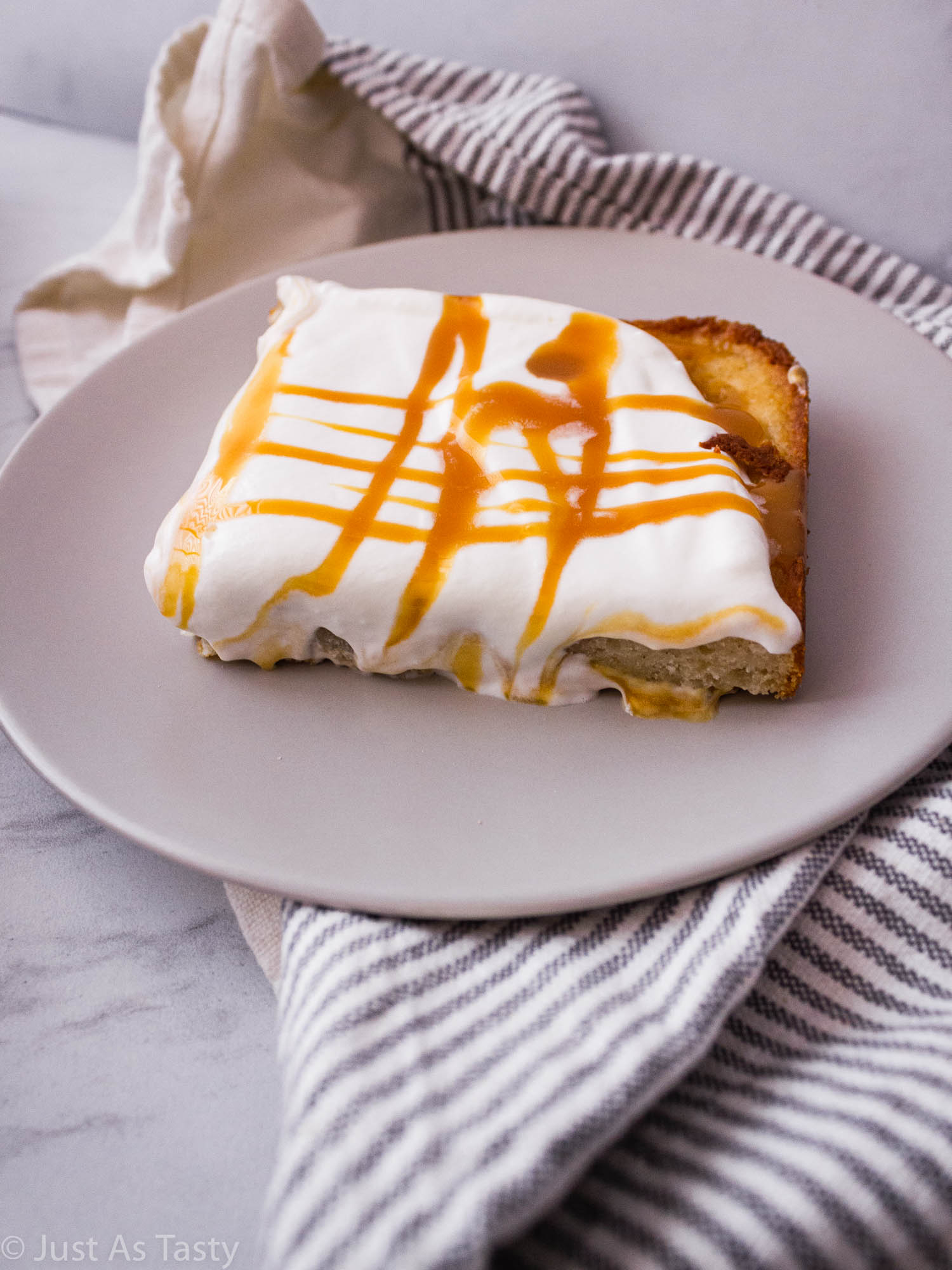 Slice of poke cake topped with whipped cream and caramel sauce. 