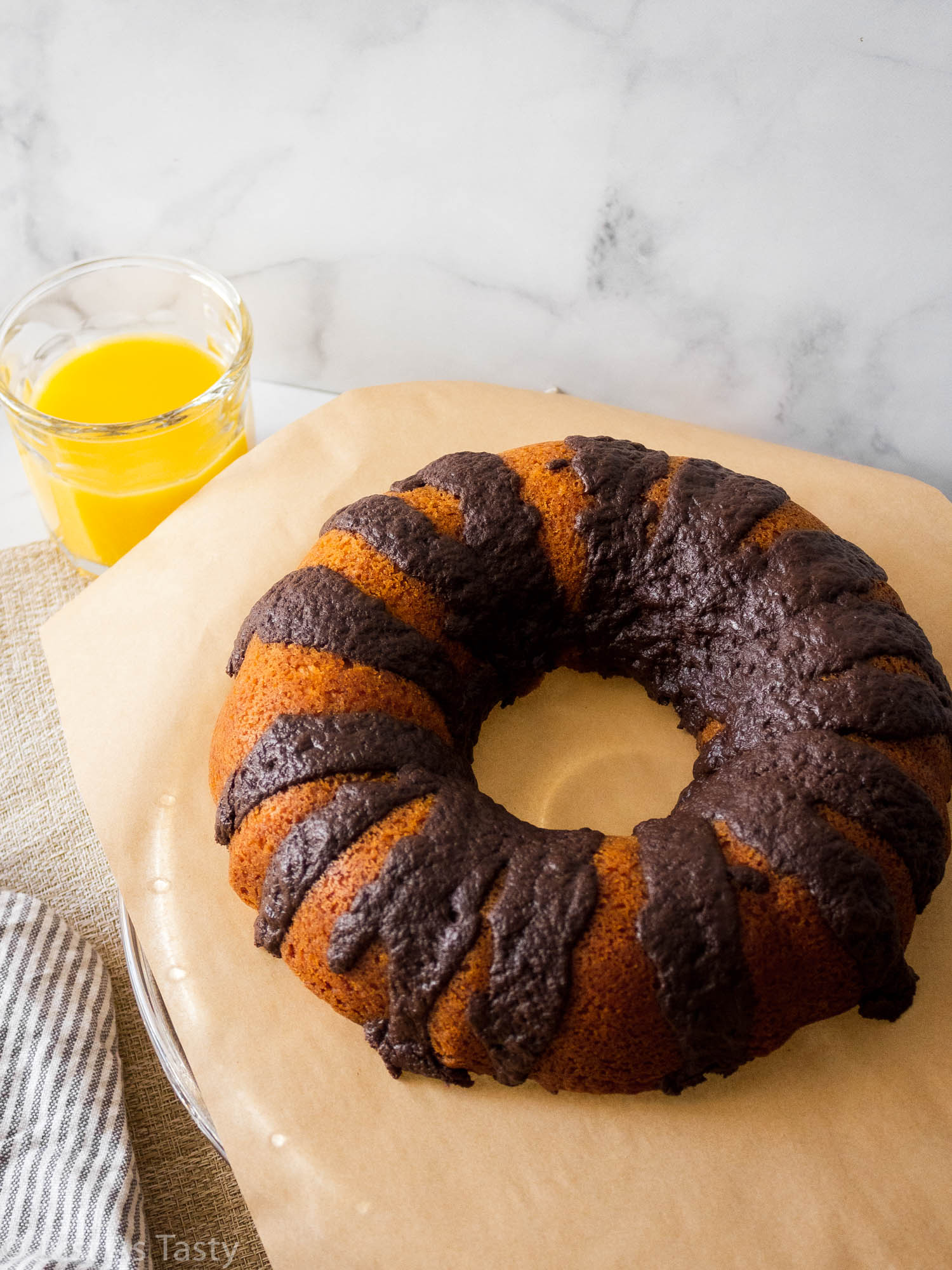 Orange bundt cake topped with chocolate drizzle on brown parchment paper. 