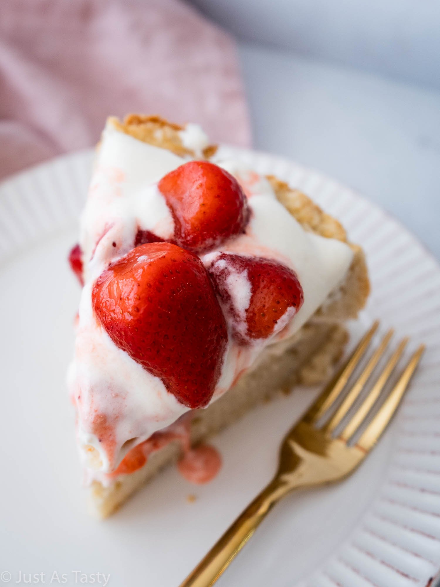 Slice of cake topped with strawberries and whipped cream on a white plate.